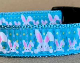 May include: A blue dog collar with a white bunny rabbit pattern and yellow stars. The collar has a silver D-ring and a black tag that says "Wag Tail Colors".