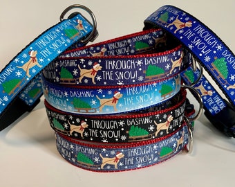 Puede incluir: Una pila de collares de perro coloridos con un tema navideño. Los collares son azules, rojos y negros con un fondo blanco. Los collares muestran un perro tirando de un trineo con un árbol de Navidad. El texto en los collares dice "Through Dashing The Snow!"