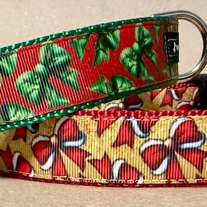 Puede incluir: Dos collares para mascotas con patrones de lazos festivos. El collar superior tiene un fondo rojo con lazos verdes y una anilla en D plateada. El collar inferior tiene un fondo dorado con lazos rojos y blancos, una hebilla negra y una anilla en D.