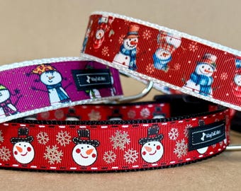May include: Three pet collars featuring snowman patterns. One collar is magenta with snowmen, while two are red with snowmen and snowflake designs. Each collar includes a black buckle, a metal D-ring, and a small black tag labeled Dog Collars.