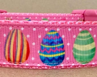 May include: Pink dog collar with a white polka dot pattern and colorful Easter egg designs. The collar has a silver D-ring and a plastic buckle.