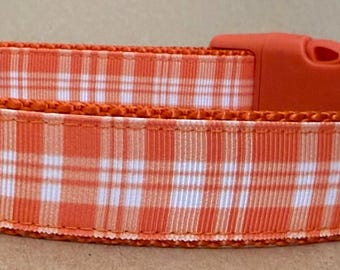 May include: Orange and white plaid dog collar with a red plastic buckle and a silver D-ring. The collar has a black label with the word "Pawsitive" on it.