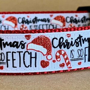 Puede incluir: Collar de perro rojo y blanco con fondo blanco e impresión navideña roja y blanca. La impresión incluye gorros de Papá Noel, bastones de caramelo y el texto "Christmas is so fetch". El collar tiene una hebilla negra y un anillo en D plateado. El collar también tiene una etiqueta negra con texto blanco que dice "Wag Tail Collars".