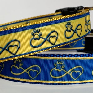 May include: Two dog collars with a yellow and blue pattern featuring paw prints and infinity symbols. The collars are made of a durable nylon material and have a metal buckle.