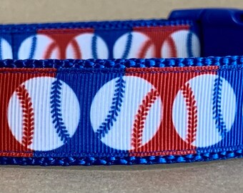 Puede incluir: Collar azul para perro con un patrón de béisbol rojo, blanco y azul. El collar tiene un anillo en D de metal y una hebilla de plástico. El collar está etiquetado como "Wag Tail Tales".