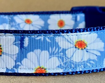 Op de afbeelding: Blauwe hondenriem met een witte margrietprint en een donkerblauwe bies. De riem heeft een zilveren D-ring en een zwart label met de tekst "Wag'n Tails".