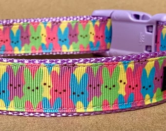 May include: Purple dog collar with a pastel Peeps pattern and a silver buckle. The collar has a black tag with the text "Pawsitive" on it.