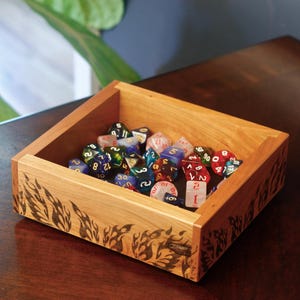 Puede incluir: Una caja de madera con un diseño de llamas en los lados, llena de dados de colores. Los dados son de plástico transparente con números rojos.