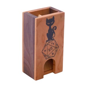 Peut inclure: Une tour à dés en bois avec une silhouette de chat noir assise sur un dé à 20 faces. La tour a une fente pour lancer les dés.