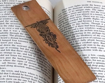 Puede incluir: Un marcapáginas de madera con una ilustración en blanco y negro de un pulpo estilizado con tentáculos. El marcapáginas está hecho de madera marrón claro y tiene un acabado liso y pulido.
