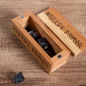 May include: A wooden box with a hinged lid, engraved with the word "remarkable" in runic script. The box is open, revealing a set of black and silver dice inside.