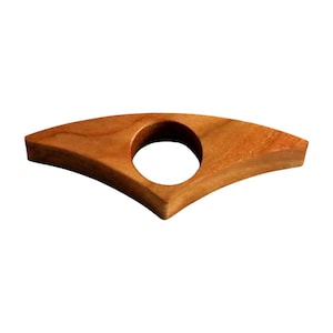 May include: A wooden book page holder with a natural finish. The holder has a curved, wing-like shape with a circular hole in the center for the thumb. The wood grain is visible, adding to its rustic charm. This reading accessory is designed to keep pages open.