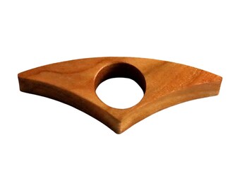 Puede incluir: Un sujetapáginas de madera con acabado natural. El soporte tiene una forma curva, similar a un ala, con un agujero circular en el centro para el pulgar. La veta de la madera es visible, lo que añade encanto rústico. Este accesorio de lectura está diseñado para mantener las páginas abiertas.