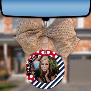 May include: A red and white polka dot car air freshener with a blue and white striped border. The air freshener has a photo of a young woman with the text "Senior 2023" written in black.