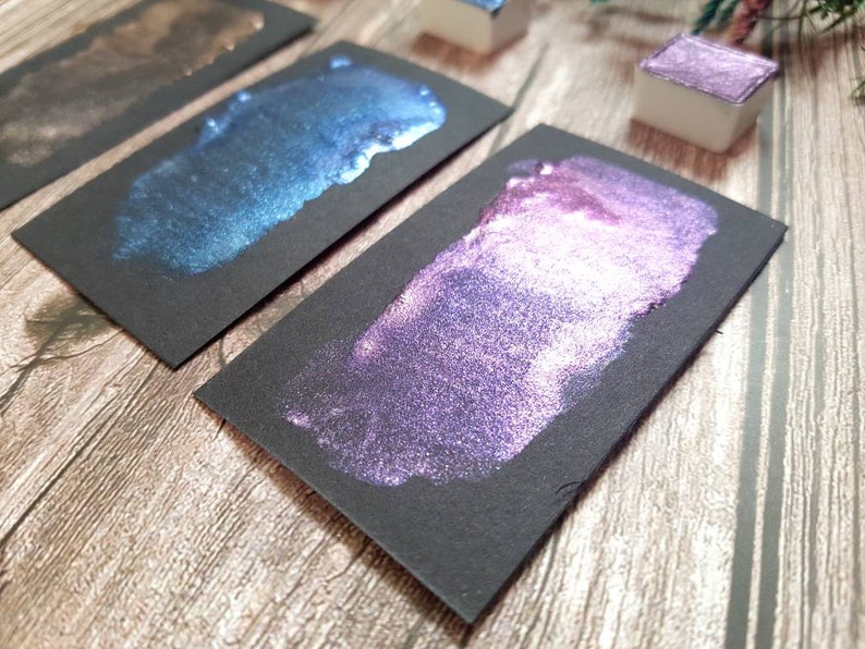 May include: Three black cardstock swatches with metallic paint samples. The swatches show a dark brown, a teal blue, and a purple with a pink shimmer.