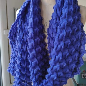 May include: A blue knitted scarf with a textured, waffle-like pattern. The scarf is folded and draped over a dress form.