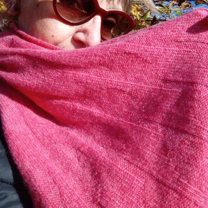 Puede incluir: Primer plano de una bufanda de punto rosa con textura de canalé. La bufanda está drapeada sobre la cabeza y los hombros de una persona.