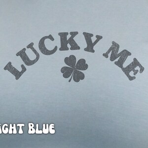 Close-up of the women's baby tee crop top in light blue. The shirt has a distressed design of a four-leaf clover and says, "Lucky Me."