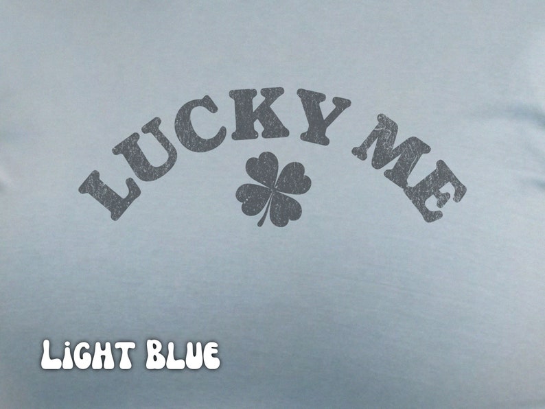 Close-up of the women's baby tee crop top in light blue. The shirt has a distressed design of a four-leaf clover and says, "Lucky Me."