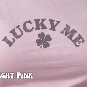 Close-up of the women's baby tee crop top in light pink. The shirt has a distressed design of a four-leaf clover and says, "Lucky Me."