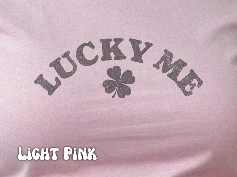 Close-up of the women's baby tee crop top in light pink. The shirt has a distressed design of a four-leaf clover and says, "Lucky Me."