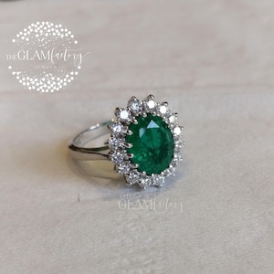 May include: A silver ring featuring a large oval emerald green gemstone encircled by a halo of smaller clear gemstones.