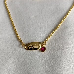Puede incluir: Un brazalete de cadena dorada con un pequeño dije ovalado grabado con el nombre "Pehali" y una piedra preciosa roja.