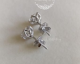 May include: A pair of silver stud earrings with clear cubic zirconia stones. The stones are set in a prong setting and have a round shape. The earrings are designed with a classic and elegant style.