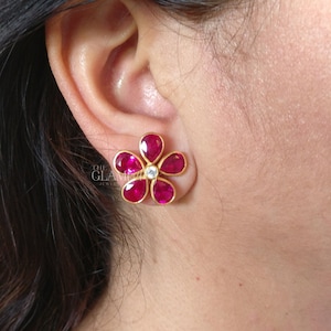 Puede incluir: Pendientes de oro en forma de flor con piedras preciosas rojas y una sola piedra preciosa blanca en el centro.