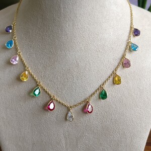 Puede incluir: Un collar de cadena dorada con piedras preciosas en forma de lágrima en varios colores, incluyendo morado, azul, verde, amarillo, rosa y rojo.