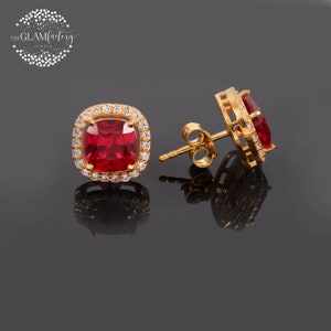 Puede incluir: Un par de pendientes de oro con una piedra preciosa cuadrada roja rodeada de un halo de piedras blancas más pequeñas.