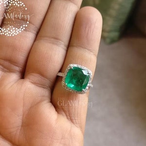 Puede incluir: Un anillo de plata con una gran piedra preciosa cuadrada de color verde esmeralda rodeada de piedras preciosas más pequeñas y transparentes.