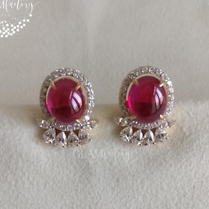 Può includere: Un paio di orecchini a lobo con grandi pietre preziose rotonde color rosso rubino. Ogni orecchino è circondato da un alone di piccoli cristalli trasparenti e incastonato in metallo dorato. Gli orecchini hanno un design decorativo in cristallo triangolare alla base.