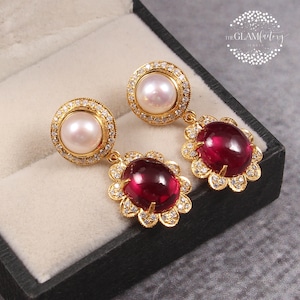 May include: Gold earrings featuring a white pearl and a red gemstone. The earrings are set in a floral design with small diamonds.