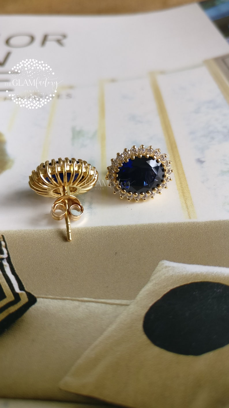 Puede incluir: Un par de pendientes de oro con una gran piedra ovalada azul rodeada de piedras peque&ntilde;as transparentes. Los pendientes tienen un cierre de poste.