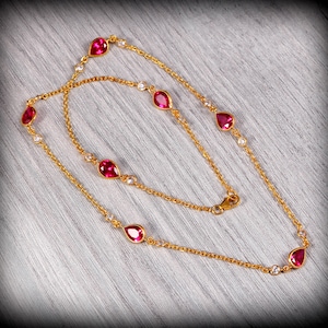 Może przedstawiać: Złoty naszyjnik z delikatnym wzorem, ozdobiony czerwonymi kamieniami szlachetnymi w kształcie łzy i małymi przezroczystymi kamieniami.