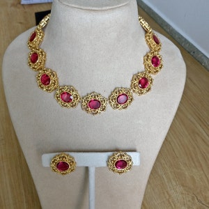May include: A gold necklace with a delicate filigree design and large red oval-shaped stones. Matching earrings with the same design and stones are also included.