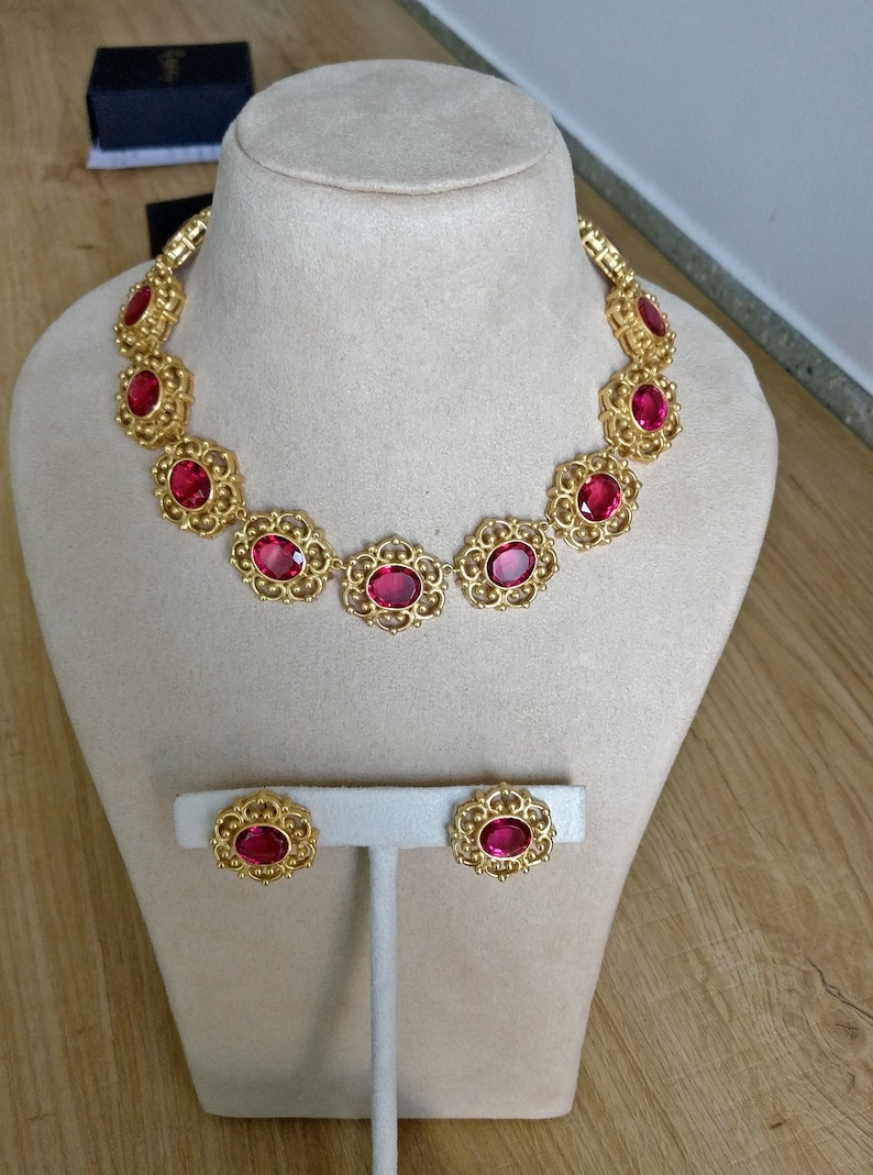 May include: A gold necklace with a delicate filigree design and large red oval-shaped stones. Matching earrings with the same design and stones are also included.