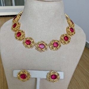 May include: A gold necklace and earrings set with large, red, oval-shaped stones set in a filigree design.