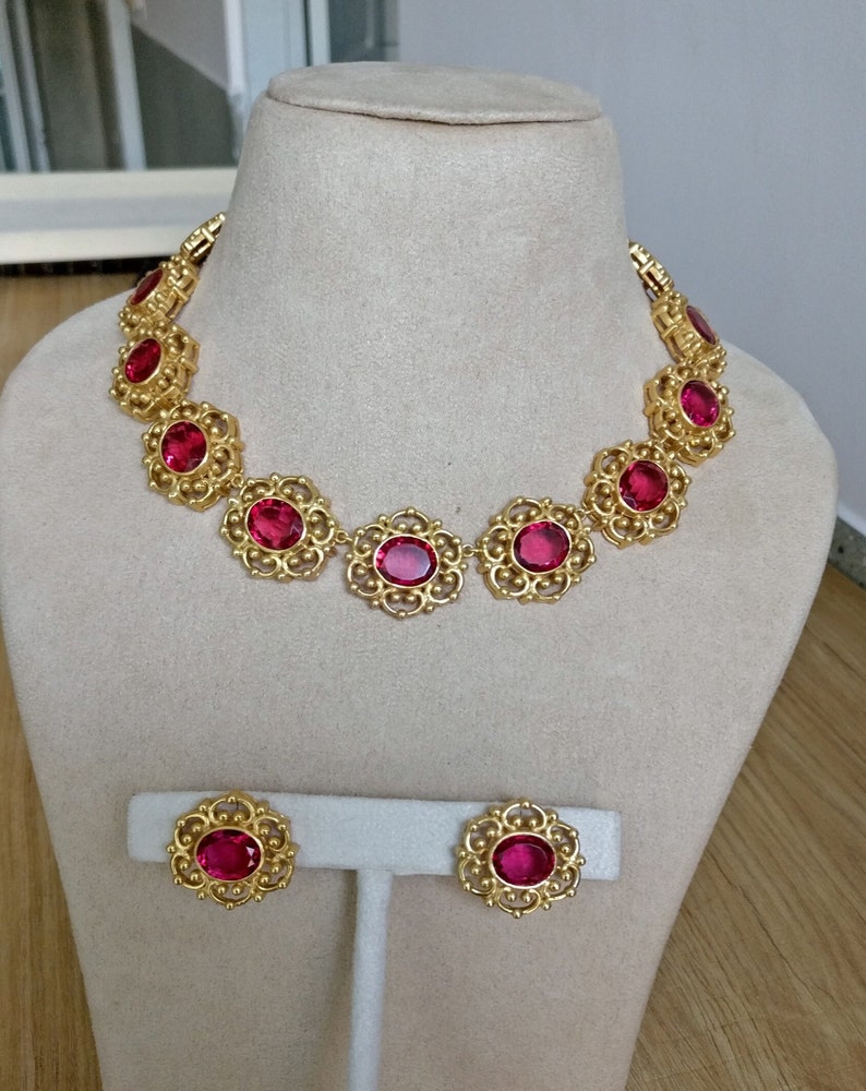 May include: A gold necklace and earrings set with large, red, oval-shaped stones set in a filigree design.