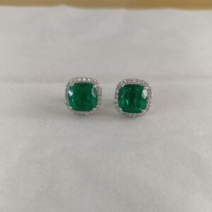 K&ouml;nnte beinhalten: Ein Paar Ohrringe aus Silber mit einem smaragdgr&uuml;nen Edelstein und einem Heiligenschein aus kleineren Diamanten.