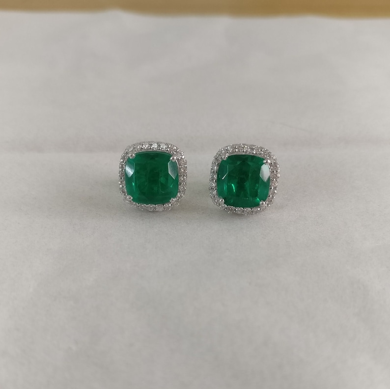 K&ouml;nnte beinhalten: Ein Paar Ohrringe aus Silber mit einem smaragdgr&uuml;nen Edelstein und einem Heiligenschein aus kleineren Diamanten.