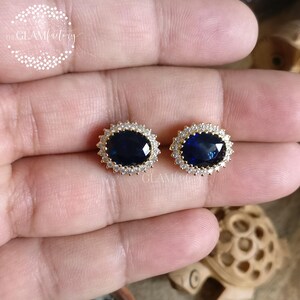 Puede incluir: Un par de pendientes de oro con una gran piedra preciosa azul rodeada de piedras preciosas transparentes m&aacute;s peque&ntilde;as.