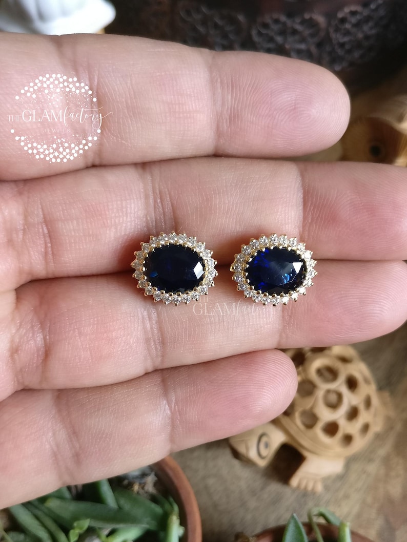 Puede incluir: Un par de pendientes de oro con una gran piedra preciosa azul rodeada de piedras preciosas transparentes m&aacute;s peque&ntilde;as.