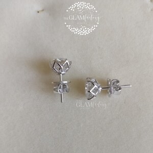 May include: A pair of silver stud earrings with a clear, round stone set in a flower-shaped design. The earrings have a post and butterfly back.