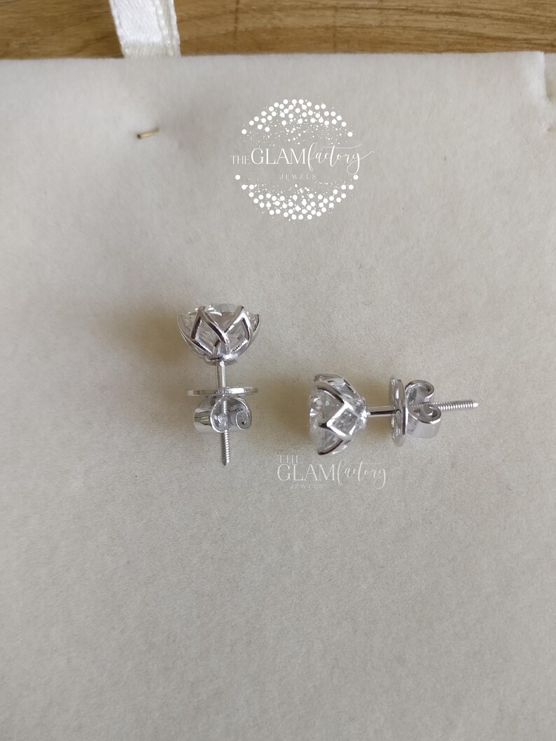May include: A pair of silver stud earrings with a clear, round stone set in a flower-shaped design. The earrings have a post and butterfly back.
