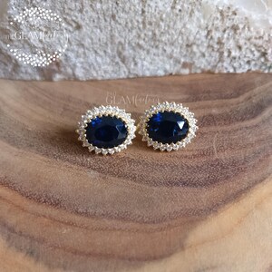 Puede incluir: Un par de pendientes de oro con una piedra ovalada azul grande rodeada de piedras peque&ntilde;as transparentes.