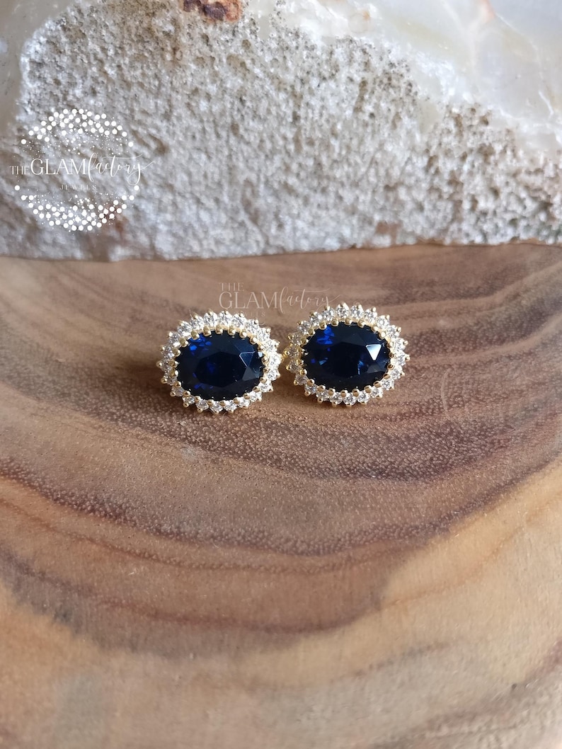 Puede incluir: Un par de pendientes de oro con una piedra ovalada azul grande rodeada de piedras peque&ntilde;as transparentes.
