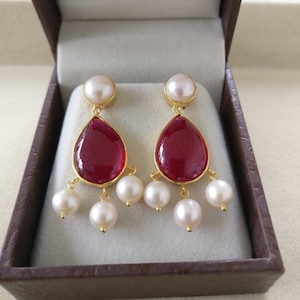 Puede incluir: Un par de pendientes de oro con piedras rojas en forma de lágrima y detalles de perlas blancas.