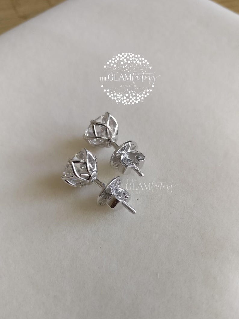 May include: A pair of silver stud earrings with clear cubic zirconia stones. The stones are set in a prong setting and have a round shape. The earrings are designed with a classic and elegant style.